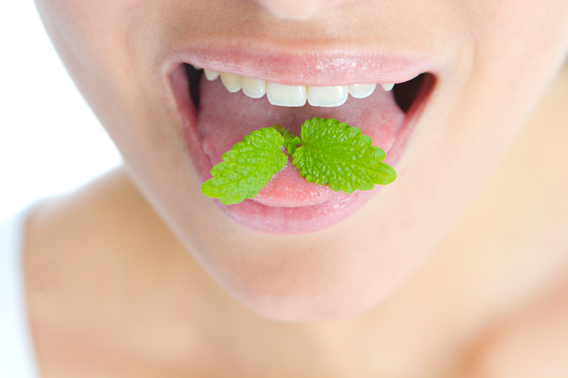 close-up picture of a mint leaf on the tounge of a womens open mouth