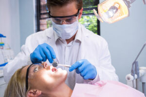 Dentist in a dental office using tools to examine a women’s mouth.